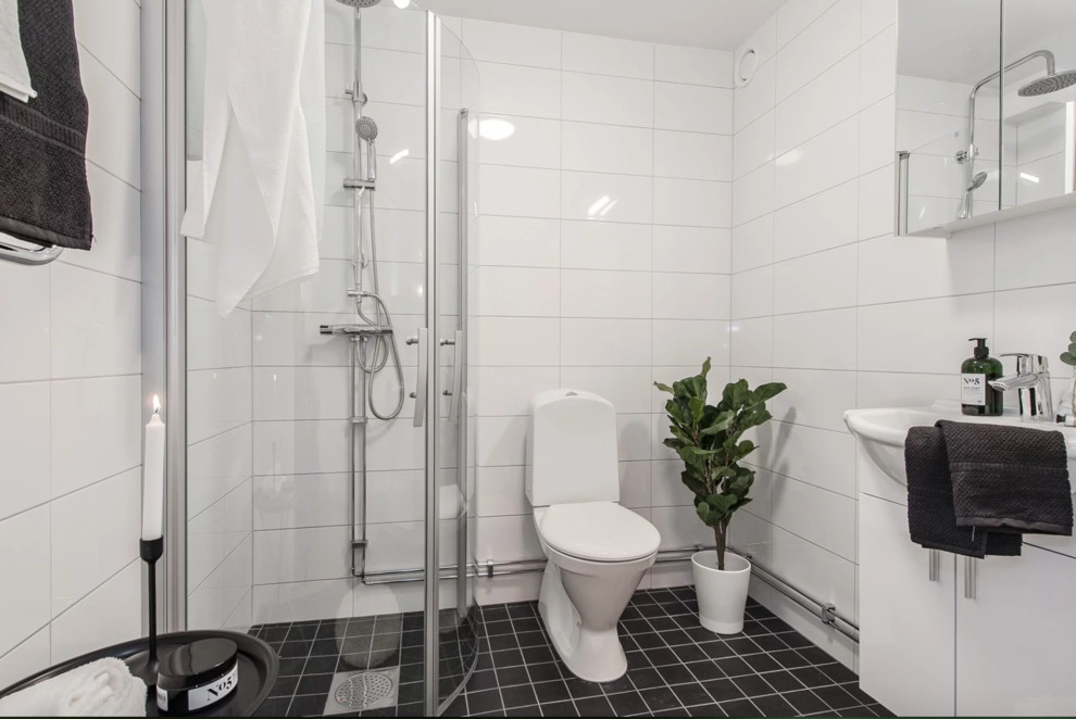 Стильный дизайн: ванная комната среднего размера в скандинавском стиле с плоскими фасадами, белыми фасадами, угловым душем, унитазом-моноблоком, белой плиткой, керамогранитной плиткой, белыми стенами, полом из керамогранита, душевой кабиной, подвесной раковиной, черным полом и душем с распашными дверями - последний тренд