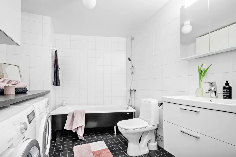 Inredning av ett klassiskt mellanstort badrum, med släta luckor, vita skåp, ett fristående badkar, en dusch/badkar-kombination, vit kakel, porslinskakel, vita väggar, ett avlångt handfat, laminatbänkskiva och svart golv
