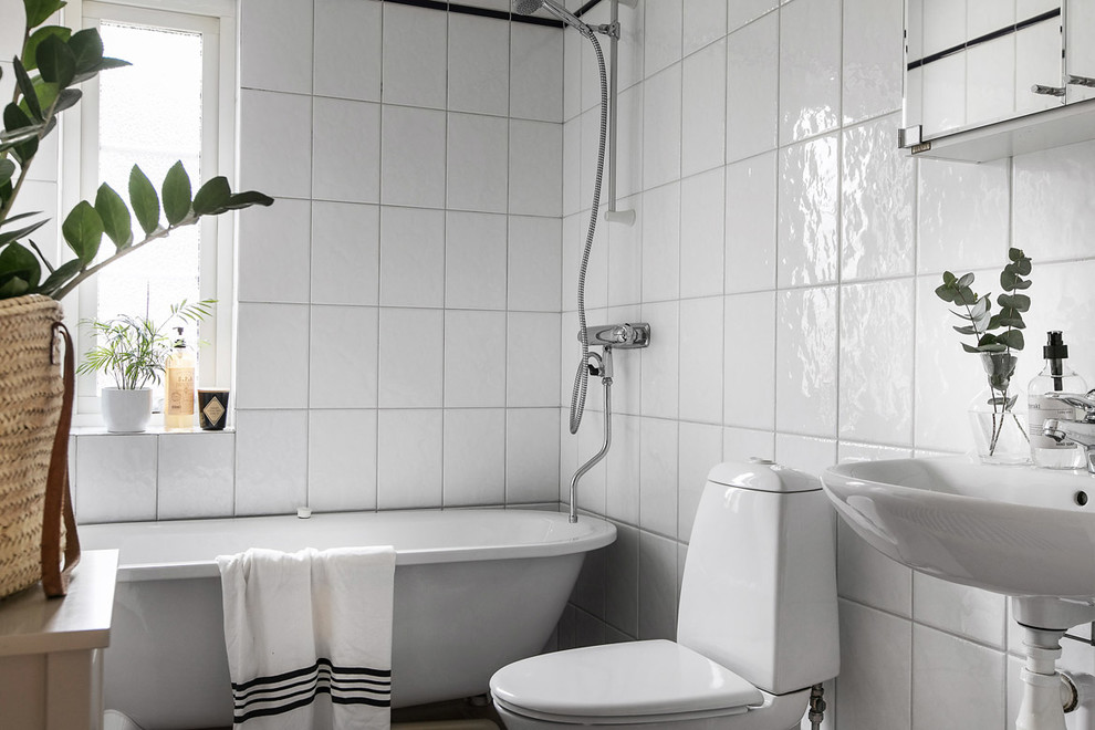 Bild på ett skandinaviskt badrum, med ett badkar med tassar, en dusch/badkar-kombination, en toalettstol med separat cisternkåpa, vit kakel, ett väggmonterat handfat och dusch med duschdraperi