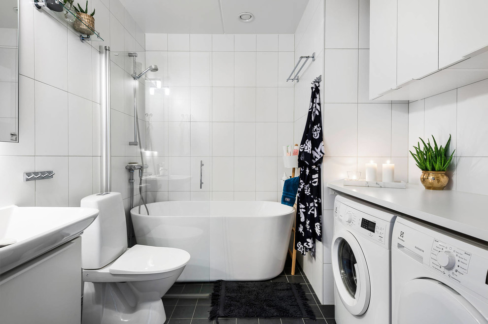 Bild på ett stort skandinaviskt vit vitt badrum, med släta luckor, vita skåp, ett fristående badkar, en kantlös dusch, vit kakel, vita väggar, ett konsol handfat, svart golv och med dusch som är öppen