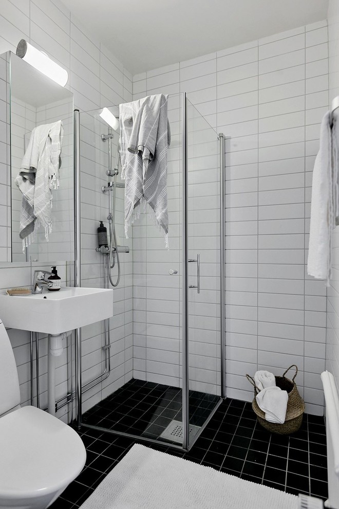 Photo of a small modern bathroom with a corner shower, white tiles, porcelain tiles, a wall-mounted sink, black floors and a hinged door.