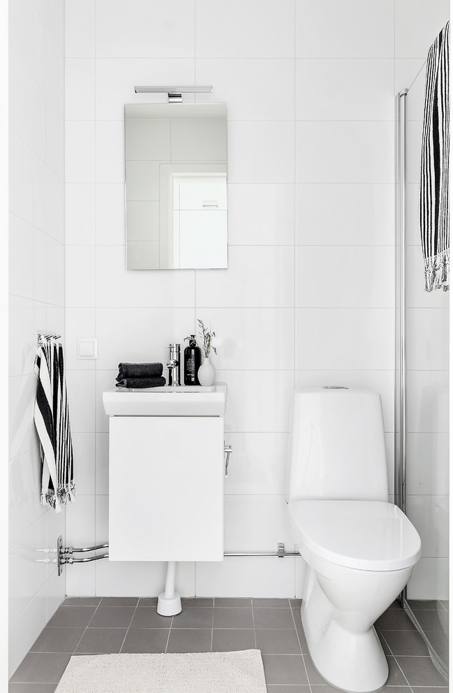 Minimalistisk inredning av ett badrum med dusch, med släta luckor, vita skåp, en hörndusch, vit kakel, vita väggar, ett konsol handfat, grått golv och dusch med gångjärnsdörr