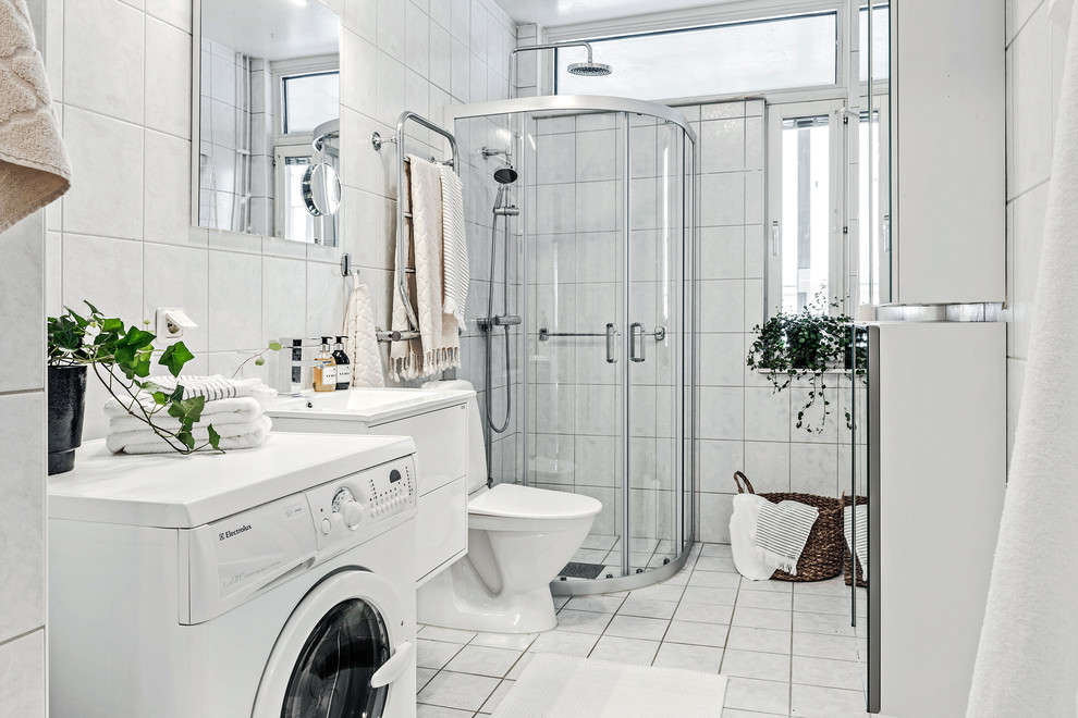 Inspiration pour une salle d'eau nordique avec une douche d'angle, une cabine de douche à porte coulissante, un placard à porte plane, des portes de placard blanches, WC à poser, un carrelage blanc, un mur blanc, un plan vasque et un sol blanc.