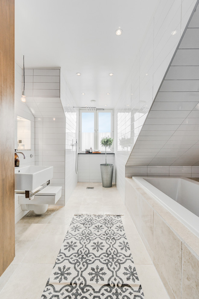Ejemplo de cuarto de baño principal, escandinavo, grande, con bañera empotrada, baldosas y/o azulejos beige, baldosas y/o azulejos blancos, paredes blancas, lavabo suspendido, sanitario de pared, baldosas y/o azulejos de porcelana, suelo de piedra caliza y suelo beige