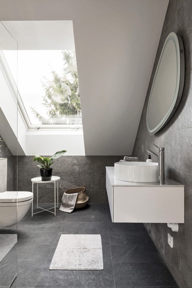 Inredning av ett minimalistiskt mellanstort vit vitt badrum med dusch, med släta luckor, vita skåp, en hörndusch, en toalettstol med hel cisternkåpa, grå kakel, ett fristående handfat och grått golv