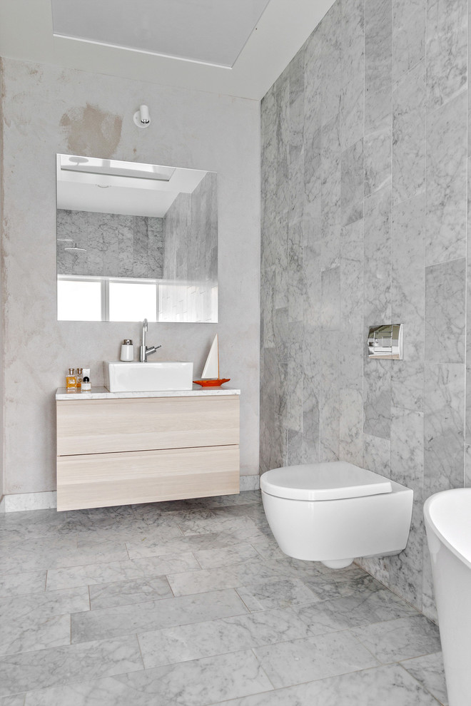 На фото: большая главная ванная комната в скандинавском стиле с плоскими фасадами, светлыми деревянными фасадами, инсталляцией, серой плиткой, мраморной плиткой, мраморным полом, настольной раковиной, отдельно стоящей ванной, душевой комнатой, серыми стенами, мраморной столешницей, серым полом и открытым душем с