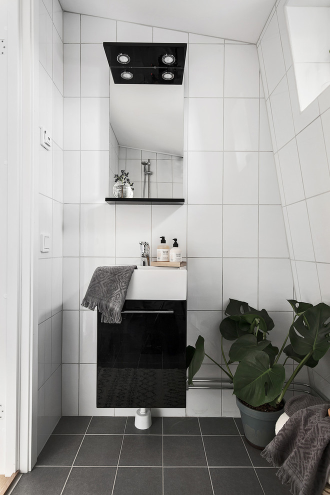 Nordisches Badezimmer mit flächenbündigen Schrankfronten, schwarzen Schränken, Keramikfliesen, weißer Wandfarbe, Keramikboden, weißen Fliesen und Wandwaschbecken in Stockholm