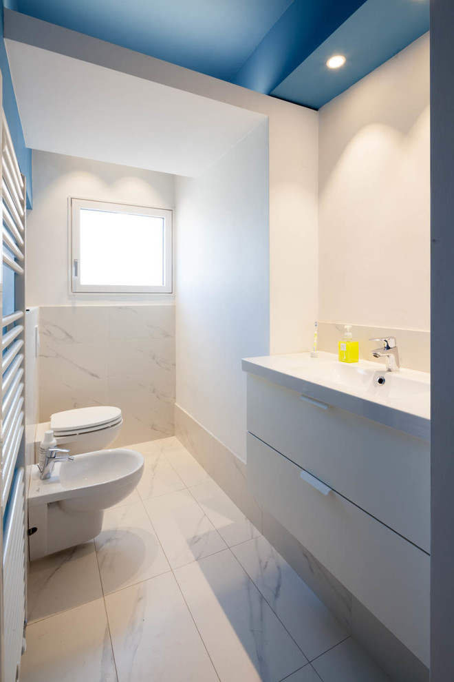 Inredning av ett modernt toalett, med släta luckor, vit kakel, vita väggar, klinkergolv i keramik, ett integrerad handfat, en bidé, stenhäll, grå skåp och vitt golv