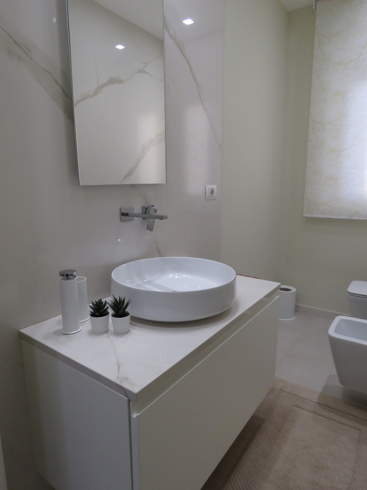 Réalisation d'un petit WC suspendu design avec un placard à porte plane, des portes de placard blanches, un carrelage blanc, des dalles de pierre, un mur beige, un sol en carrelage de porcelaine, une vasque, un plan de toilette en marbre, un sol beige et un plan de toilette blanc.