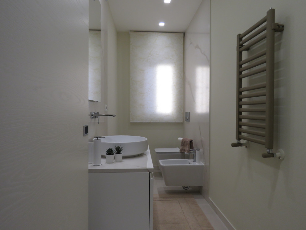 Idéer för att renovera ett litet funkis vit vitt toalett, med släta luckor, vita skåp, en vägghängd toalettstol, vit kakel, stenhäll, beige väggar, klinkergolv i porslin, ett fristående handfat, marmorbänkskiva och beiget golv