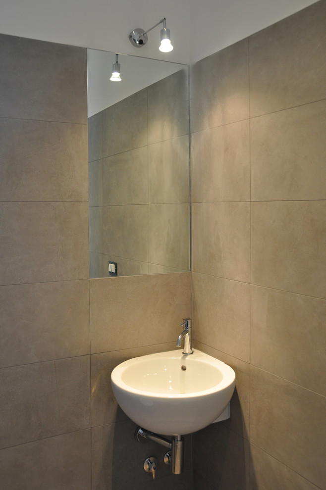Foto på ett litet funkis toalett, med porslinskakel, klinkergolv i porslin, ett väggmonterat handfat och beige kakel