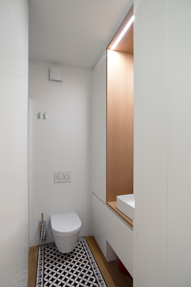Kleine Moderne Gästetoilette mit Wandtoilette, weißer Wandfarbe, hellem Holzboden, Waschtisch aus Holz, buntem Boden und brauner Waschtischplatte in Sonstige