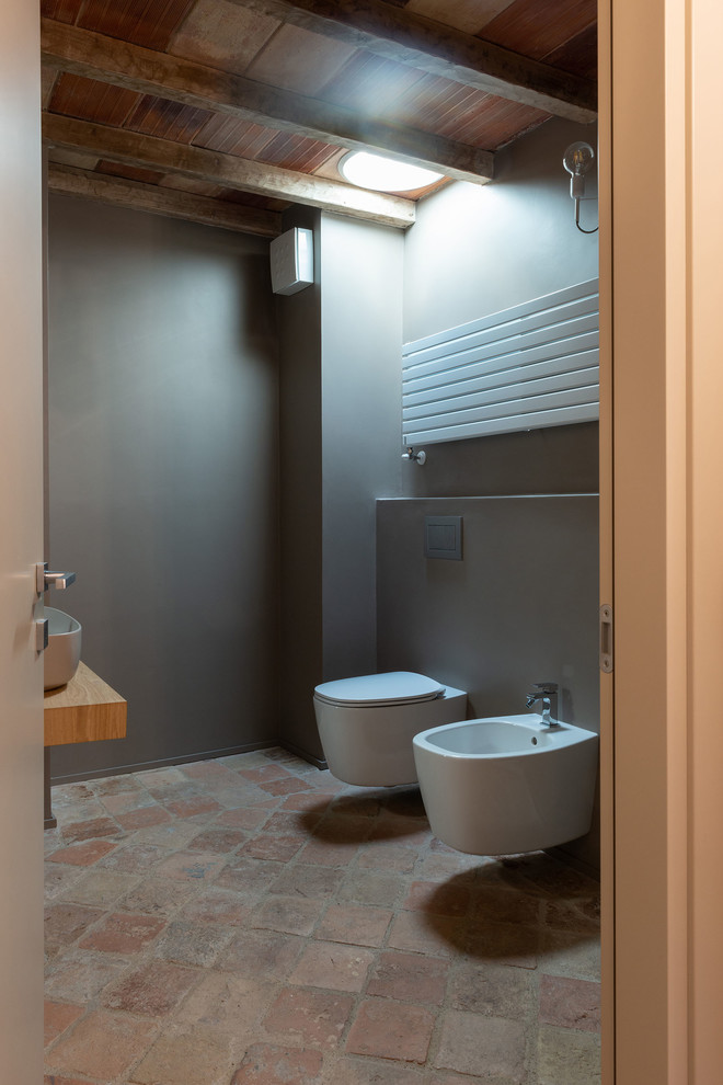 Cette image montre un WC et toilettes chalet en bois clair de taille moyenne avec WC séparés, un mur marron, tomettes au sol, une vasque, un plan de toilette en bois, un sol multicolore et un plan de toilette marron.