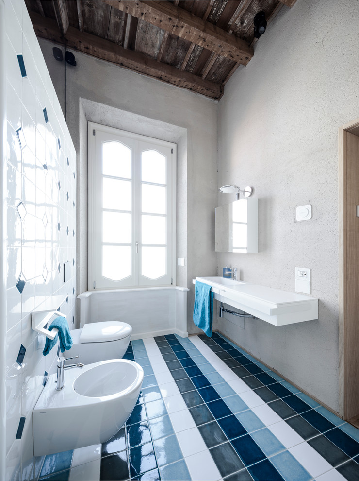 Cette image montre un WC suspendu design de taille moyenne avec un placard à porte plane, des carreaux de céramique, un mur gris, un sol en carrelage de céramique et un lavabo intégré.