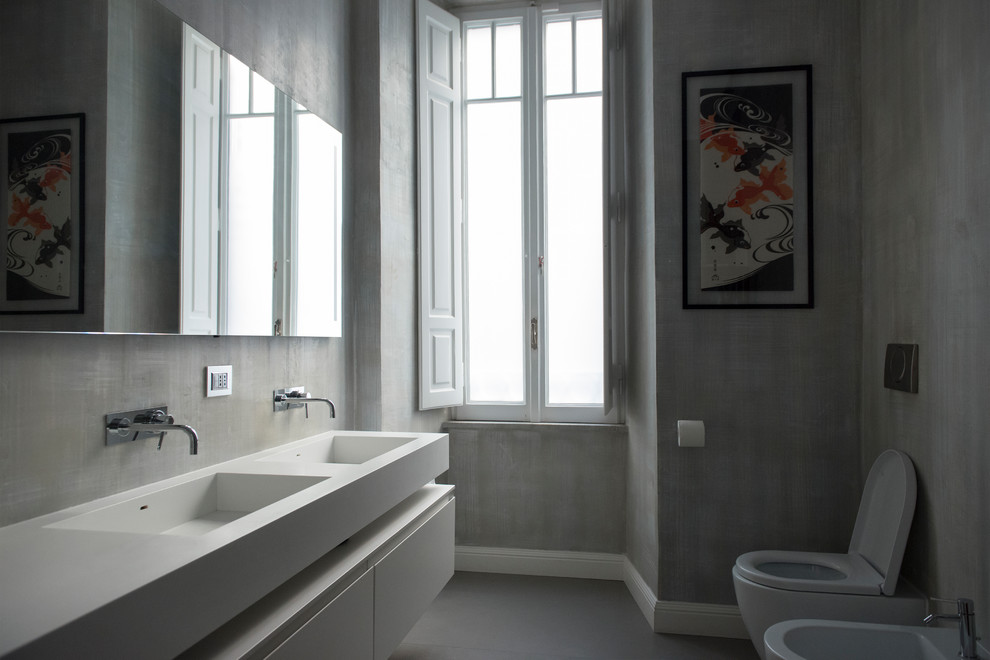 Immagine di un ampio bagno di servizio contemporaneo con ante di vetro, ante bianche, WC a due pezzi, pareti grigie, lavabo sospeso, top in superficie solida, pavimento grigio e top bianco
