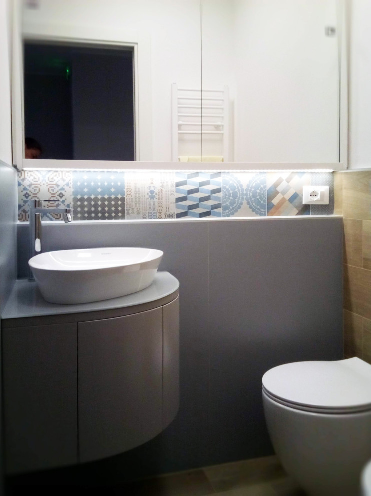 Idéer för små funkis toaletter, med luckor med profilerade fronter, en toalettstol med separat cisternkåpa, flerfärgad kakel, porslinskakel, vita väggar, klinkergolv i porslin, ett fristående handfat och bänkskiva i glas