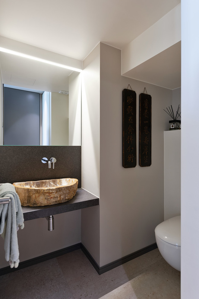 Пример оригинального дизайна: туалет в современном стиле с инсталляцией, белыми стенами, настольной раковиной, серым полом и черной столешницей