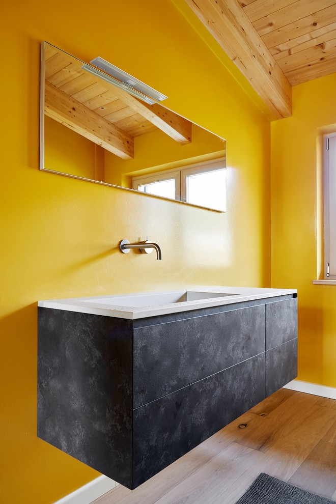 Kleine Moderne Gästetoilette mit flächenbündigen Schrankfronten, grauen Schränken, gelber Wandfarbe, braunem Holzboden, Einbauwaschbecken und beigem Boden in Sonstige