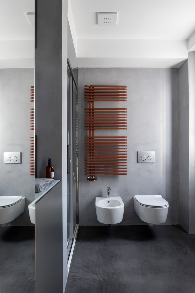 Cette photo montre un WC suspendu tendance de taille moyenne avec un placard à porte plane, des portes de placard noires, un mur gris, sol en béton ciré, un lavabo suspendu et un sol gris.