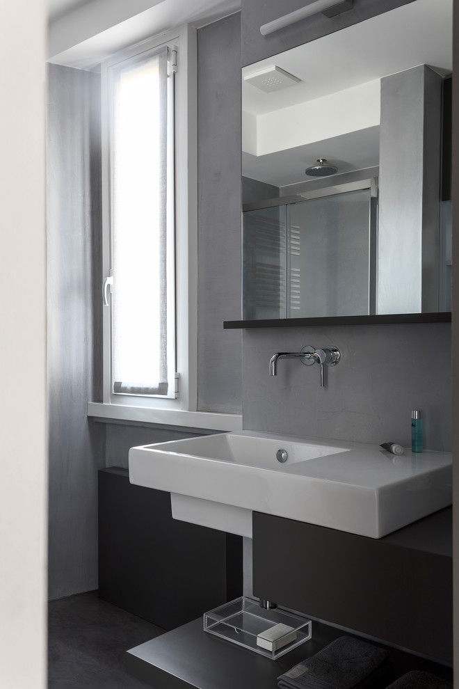 Idee per un bagno di servizio minimal di medie dimensioni con ante lisce, ante nere, pareti grigie, pavimento in cemento, lavabo sospeso, top in superficie solida, pavimento grigio e top bianco