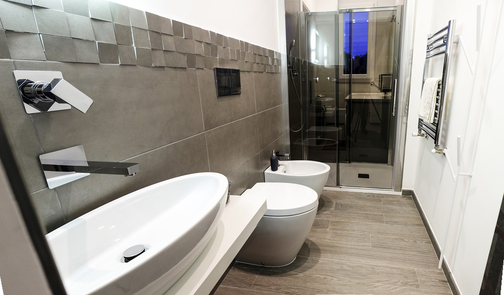 Bild på ett litet funkis badrum, med en toalettstol med separat cisternkåpa, grå kakel, porslinskakel, vita väggar, klinkergolv i porslin, ett fristående handfat, träbänkskiva och grått golv