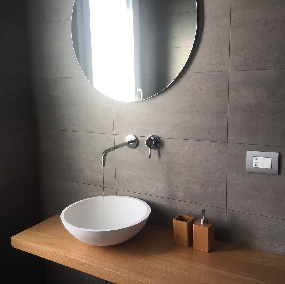 Réalisation d'un petit WC et toilettes minimaliste en bois clair avec WC séparés, un carrelage gris, des carreaux de porcelaine, un mur gris, un sol en carrelage de porcelaine, une vasque, un plan de toilette en bois et un sol gris.