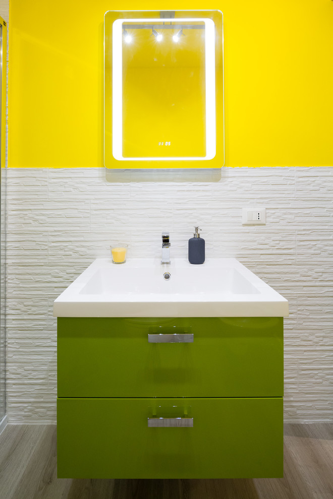 Kleine Moderne Gästetoilette mit offenen Schränken, grünen Schränken, Toilette mit Aufsatzspülkasten, weißen Fliesen, Porzellanfliesen, gelber Wandfarbe, braunem Holzboden, Einbauwaschbecken, Mineralwerkstoff-Waschtisch und grauem Boden in Mailand