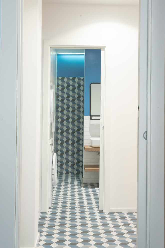 Modern inredning av ett litet toalett, med skåp i ljust trä, en toalettstol med separat cisternkåpa, blå kakel, porslinskakel, blå väggar, klinkergolv i porslin, ett fristående handfat, träbänkskiva och blått golv