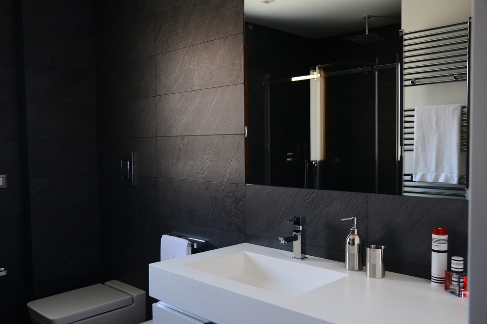 Mid-sized trendy black tile and porcelain tile powder room photo in Catania-Palermo with white cabinets, a two-piece toilet, white walls, solid surface countertops and an integrated sink