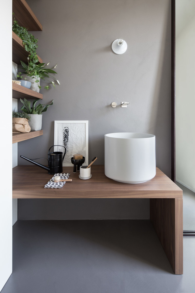 Inredning av ett minimalistiskt brun brunt toalett, med grå väggar, ett fristående handfat, träbänkskiva och grått golv