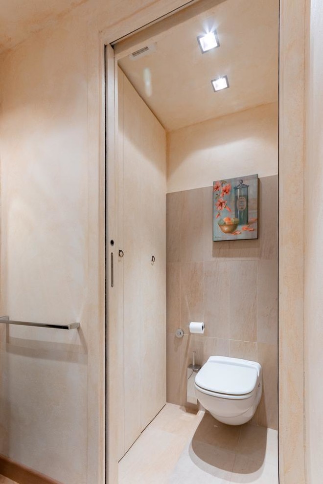 Example of a small mountain style beige tile and porcelain tile porcelain tile and beige floor powder room design in Other with flat-panel cabinets, beige cabinets, a wall-mount toilet and beige walls