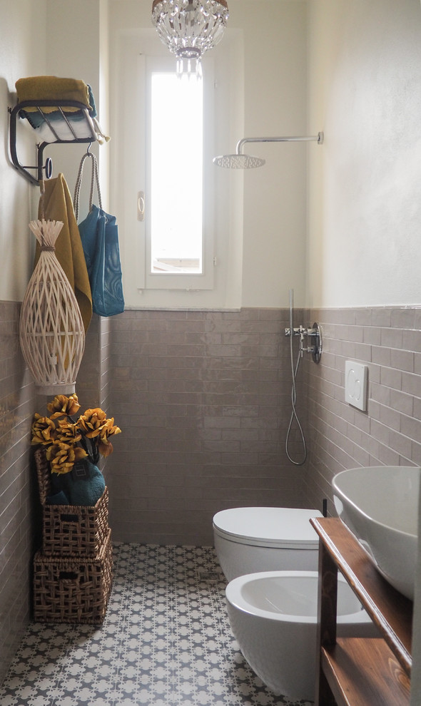 Foto på ett litet nordiskt toalett, med skåp i mörkt trä, en vägghängd toalettstol, grå kakel, keramikplattor, vita väggar, cementgolv, ett fristående handfat och träbänkskiva