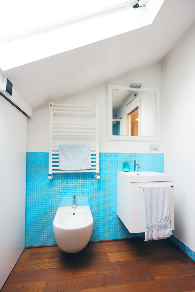 Kleine Moderne Gästetoilette mit weißen Schränken, blauen Fliesen, weißer Wandfarbe, flächenbündigen Schrankfronten, Bidet, Mosaikfliesen und braunem Holzboden in Sonstige