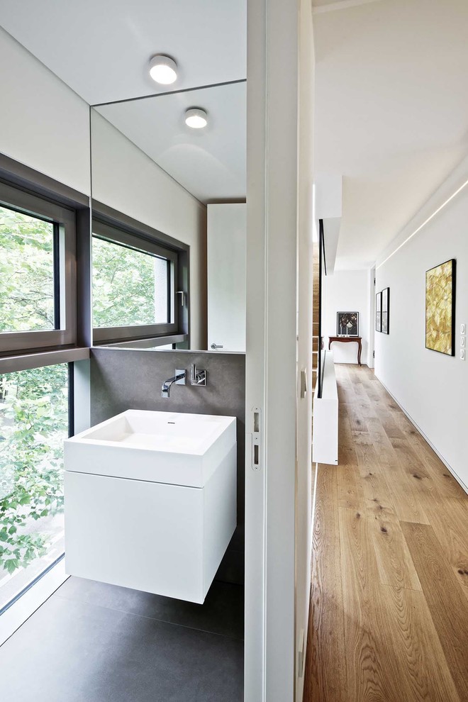 Aménagement d'un WC et toilettes moderne avec un placard à porte plane, des portes de placard blanches, un mur blanc, un plan vasque et un sol gris.