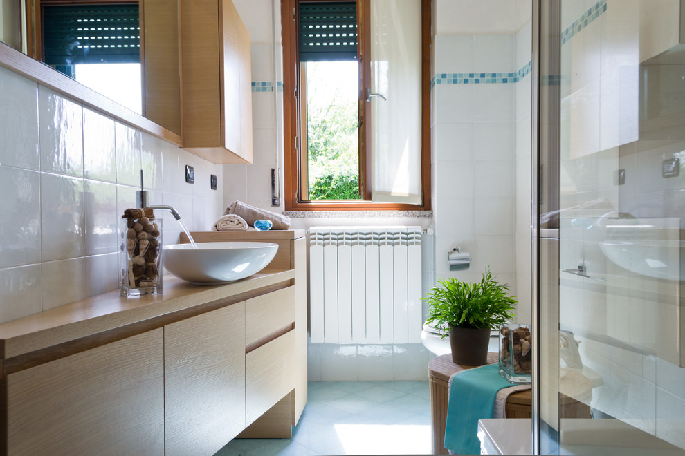 Bild på ett litet funkis toalett, med skåp i ljust trä, en toalettstol med separat cisternkåpa, vit kakel, porslinskakel, vita väggar, klinkergolv i porslin, ett fristående handfat, träbänkskiva och blått golv