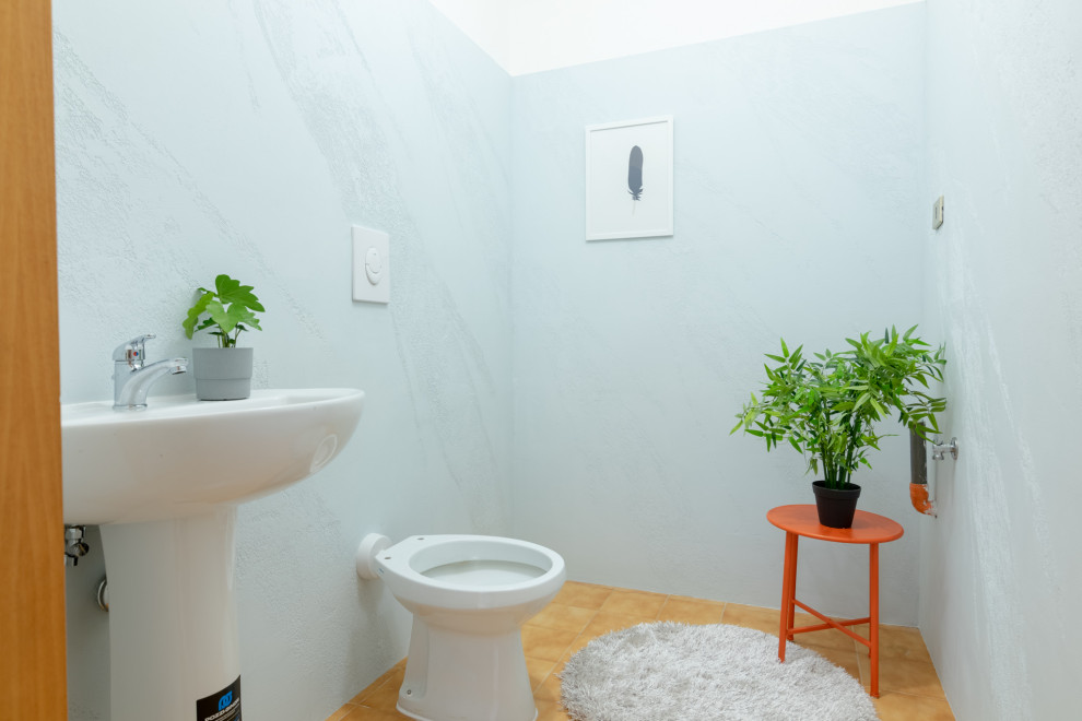 Exempel på ett litet modernt toalett, med öppna hyllor, vita skåp, en toalettstol med hel cisternkåpa, blå kakel, blå väggar, klinkergolv i porslin, ett piedestal handfat och beiget golv