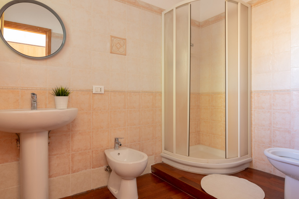 Photo of a small mediterranean cloakroom in Other with open cabinets, white cabinets, a two-piece toilet, pink tiles, ceramic tiles, white walls, dark hardwood flooring, a pedestal sink and brown floors.