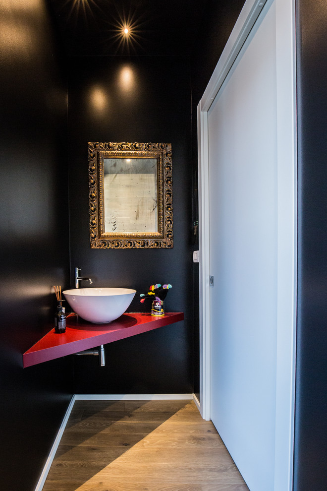 ミラノにあるコンテンポラリースタイルのおしゃれなトイレ・洗面所 (黒い壁、無垢フローリング、赤い洗面カウンター) の写真