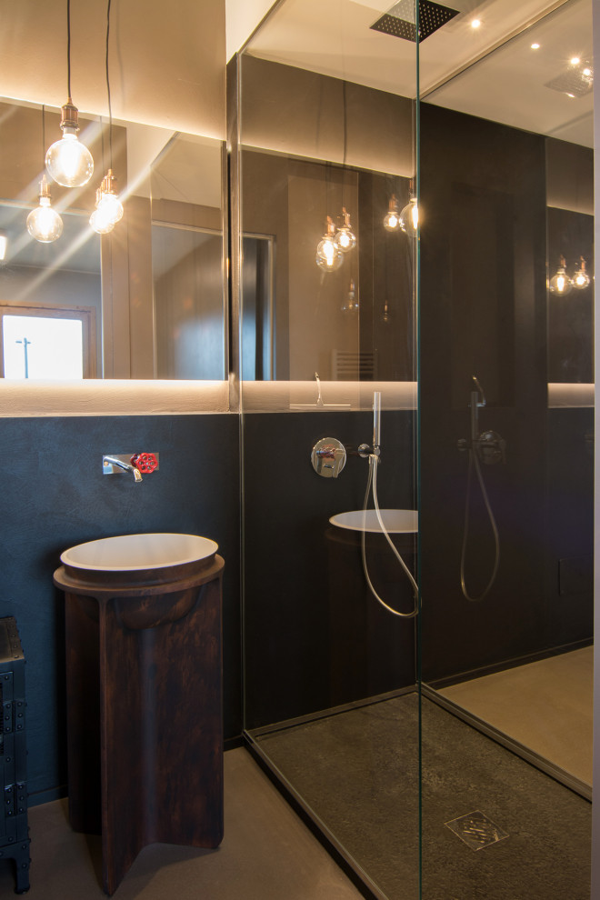 Foto på ett litet industriellt badrum, med luckor med infälld panel, svarta skåp, en toalettstol med separat cisternkåpa, svart kakel, svarta väggar, betonggolv och ett piedestal handfat