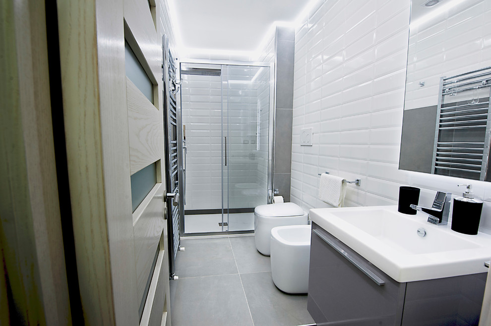 На фото: ванная комната среднего размера в стиле модернизм с плоскими фасадами, серыми фасадами, раздельным унитазом, белой плиткой, керамической плиткой, белыми стенами, полом из керамогранита, монолитной раковиной и столешницей из искусственного камня с