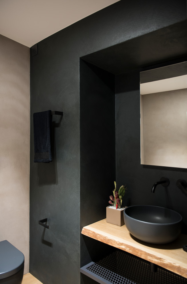 Exempel på ett mellanstort modernt toalett, med en vägghängd toalettstol, svart kakel, svarta väggar och träbänkskiva