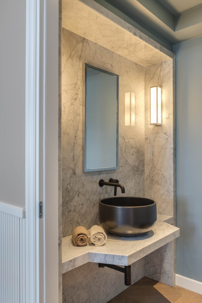 Cette photo montre un petit WC et toilettes tendance avec WC à poser, parquet clair, une vasque, un plan de toilette en marbre et un sol beige.