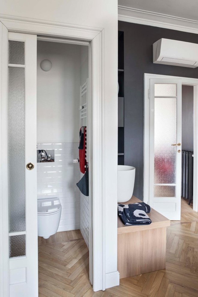 Inspiration for a contemporary cloakroom in Milan with medium wood cabinets, a wall mounted toilet, white tiles, metro tiles, white walls, light hardwood flooring, a vessel sink, wooden worktops, beige floors and brown worktops.
