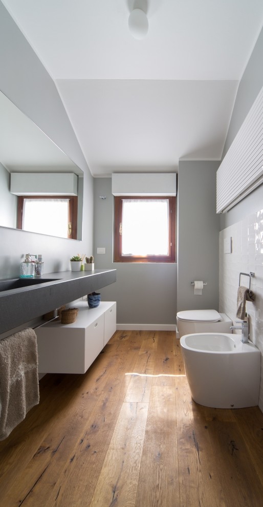 Idéer för små funkis toaletter, med släta luckor, vita skåp, en bidé, grå väggar, mellanmörkt trägolv, brunt golv, vit kakel, ett integrerad handfat och bänkskiva i betong