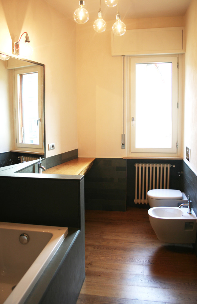 Immagine di un bagno di servizio design con WC a due pezzi, piastrelle grigie, piastrelle in pietra, pareti beige, pavimento in legno massello medio, lavabo integrato e top in legno