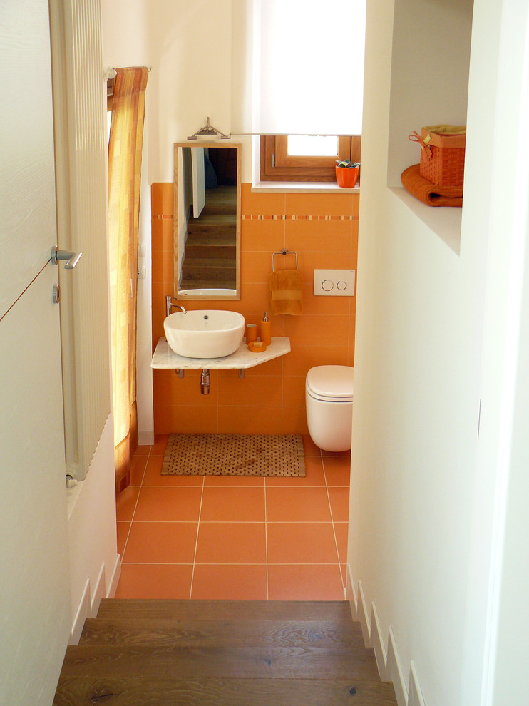 Inspiration för små moderna toaletter, med en vägghängd toalettstol, orange kakel, keramikplattor, vita väggar, klinkergolv i keramik och ett fristående handfat