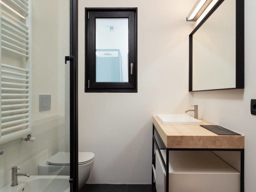 Inspiration pour un WC suspendu minimaliste de taille moyenne avec un placard à porte plane, des portes de placard blanches, un carrelage noir, du carrelage en marbre, un mur blanc, un sol en marbre, un lavabo de ferme, un plan de toilette en bois et un sol noir.