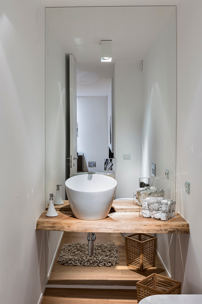 Cette photo montre un WC et toilettes tendance en bois clair de taille moyenne avec WC séparés, un carrelage blanc, des carreaux de miroir, un mur blanc, parquet clair, une vasque, un plan de toilette en bois et un plan de toilette marron.