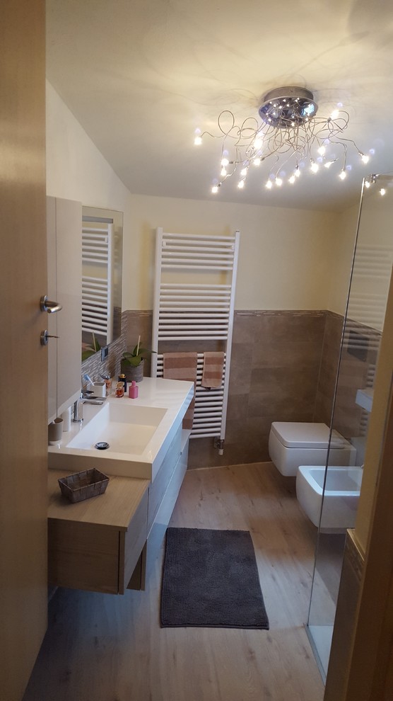 Immagine di un piccolo bagno di servizio moderno con WC sospeso, piastrelle beige, piastrelle in ceramica, pareti beige, pavimento in laminato, lavabo integrato, pavimento beige e top bianco