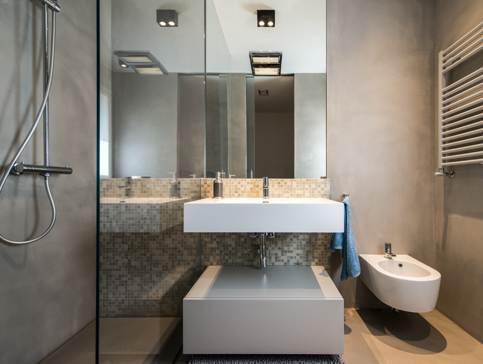 Design ideas for a small modern cloakroom in Other with flat-panel cabinets, grey cabinets, a wall mounted toilet, multi-coloured tiles, mosaic tiles, grey walls, a trough sink and beige floors.